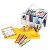 A gray felt organizer with a handle holds colored pencils, coloring books, and markers. In front, there's a yellow cup with more colored pencils on a TRUE Silicone Cloud Placemat. Scattered pencils sit on the BPA-free silicone mat nearby. A wooden block set and another coloring book complete the setup.