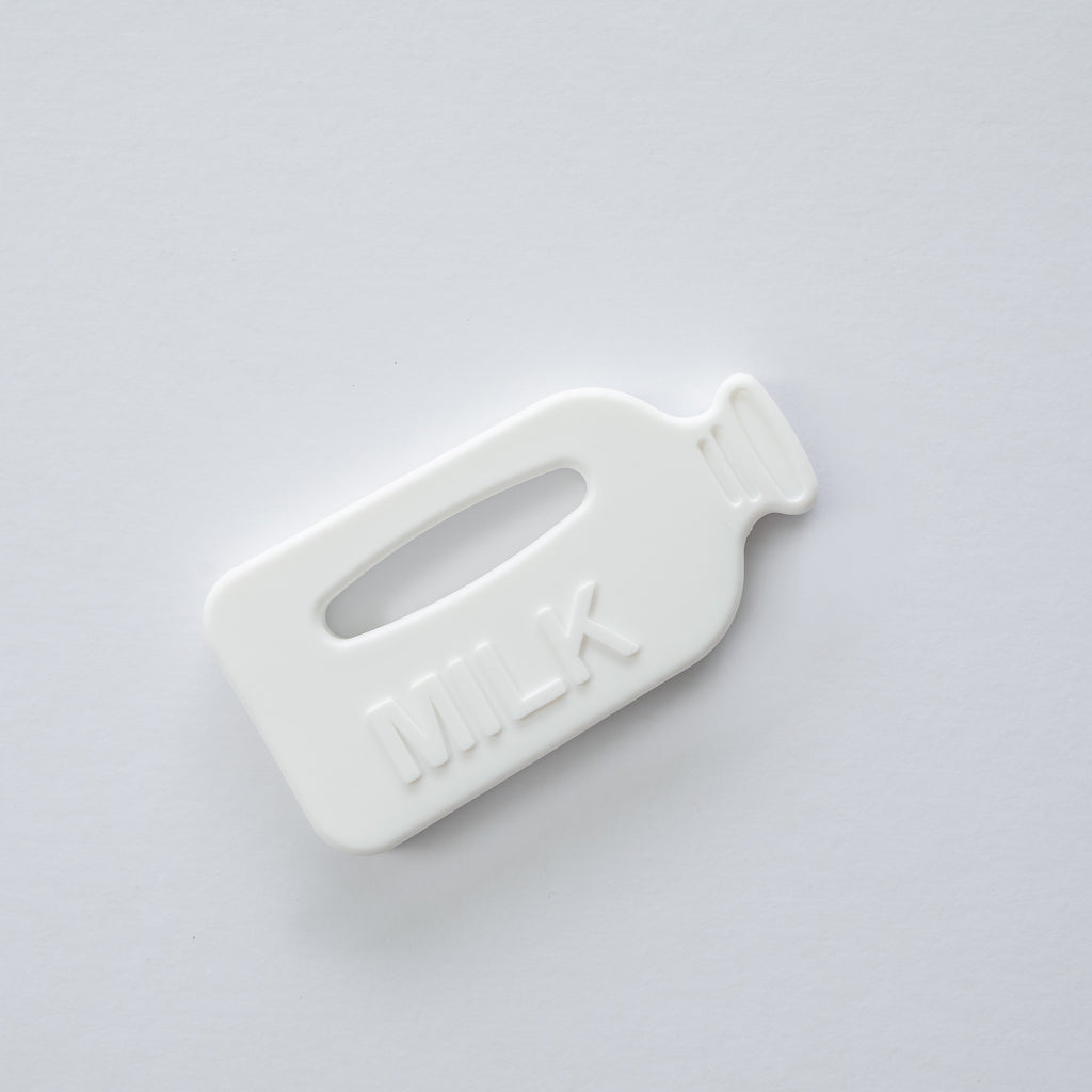 A white silicone teether designed to resemble a milk bottle with raised sensory bumps and bubbles on the reverse side.