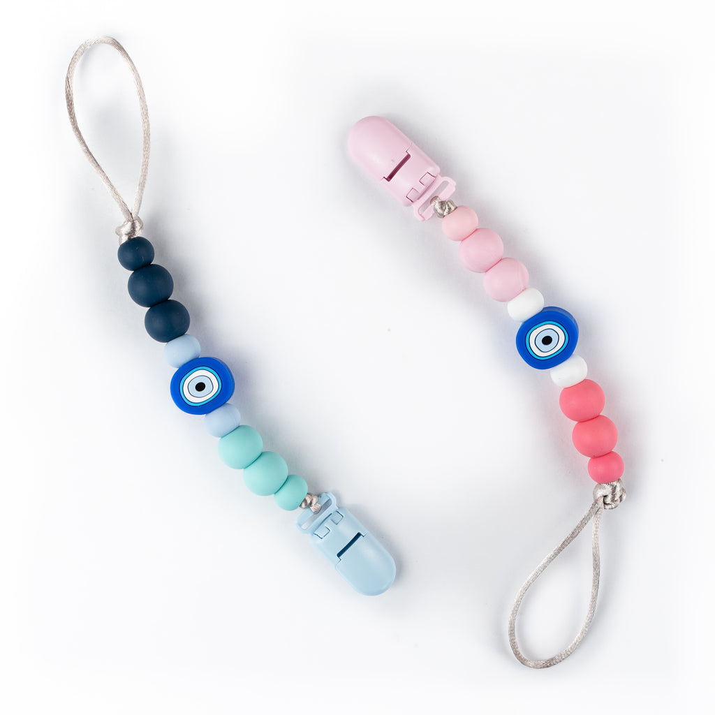 Two beaded clips with silicone beads in blue and pink colors, featuring a central talisman believed to protect against the evil-eye. One clip has a loop attached, presumably for holding an item like a pacifier or teether.